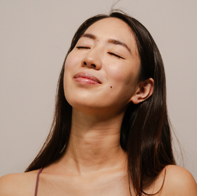 Portrait of a relaxed young woman with eyes closed, glowing skin and long dark hair, natural skincare and wellness vibe