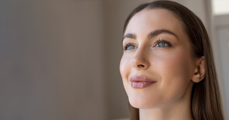 Close-up portrait of a woman with clear skin and natural makeup looking upward in soft natural light