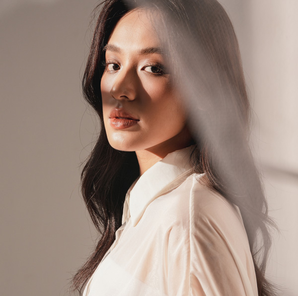 Elegant portrait of a woman in soft light wearing a white blouse, looking over her shoulder with natural makeup
