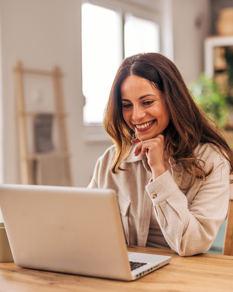 Woman smiling at laptop in cozy home office, remote work or video call