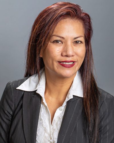 Professional headshot of a smiling woman with long dark hair wearing a pinstripe blazer and white blouse