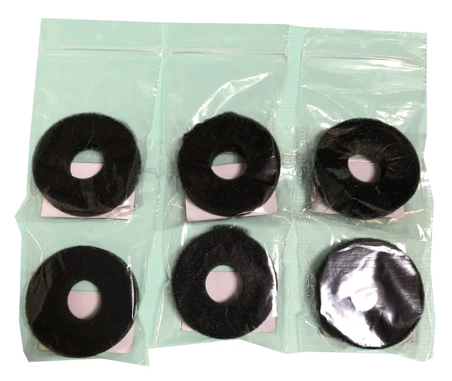 Six black donut-shaped hair bun pads in individual clear plastic bags on a mint background